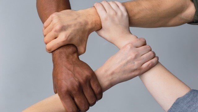 4人の異なる人種の人々が手を取り合っている手元のアップ写真。